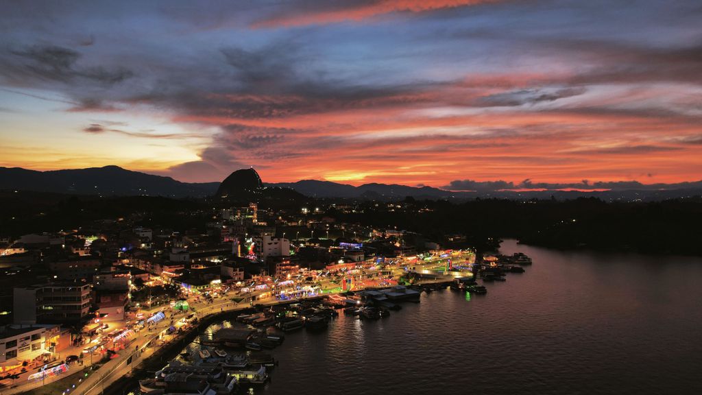 Aerial view of Guatapé, Colombia at sunset with colorful lights reflecting on the water.