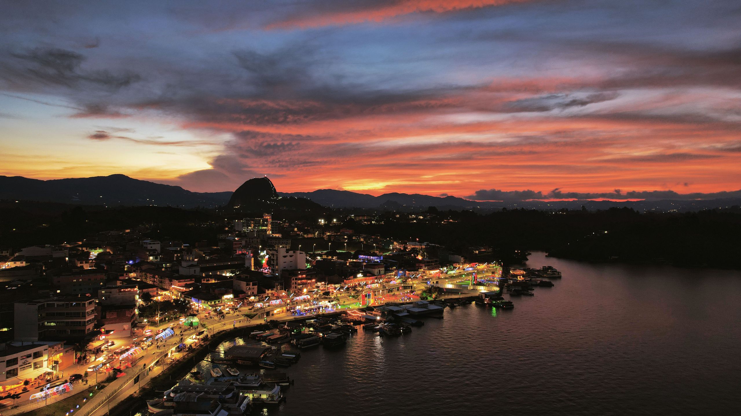 Aerial view of Guatapé, Colombia at sunset with colorful lights reflecting on the water.