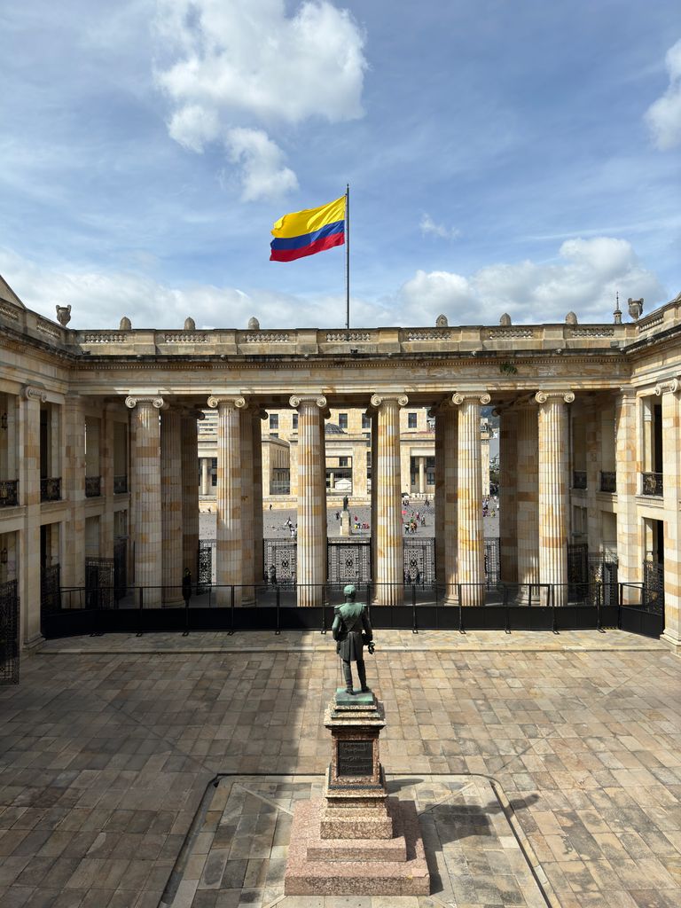 The Colombian flag waves above a historic courtyard in Bogotá, Colombia, under a clear sky.