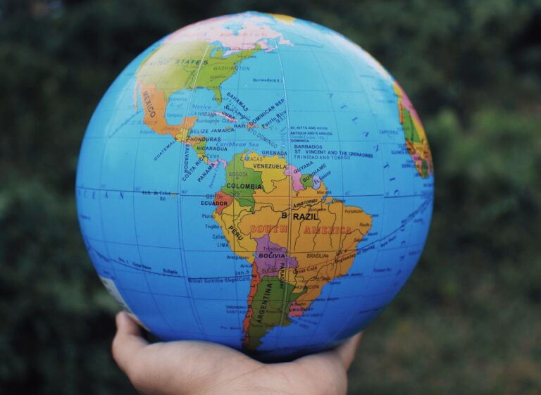 Crop anonymous person reaching out hand and showing Earth globe against green plants in daytime